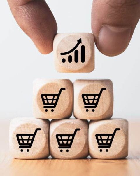 a hand holding a wooden block with a shopping cart and a graph, illustrating one way to increase sales.