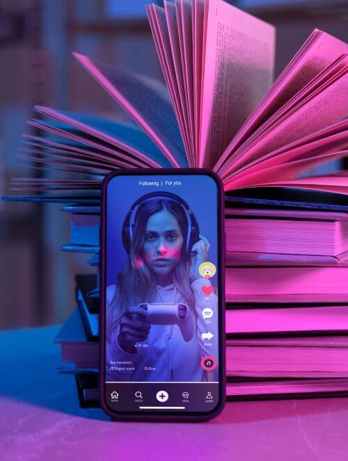 smartphone displaying a social media video of a young woman, surrounded by a stack of open pink books with neon lighting, offering free advice on making money.