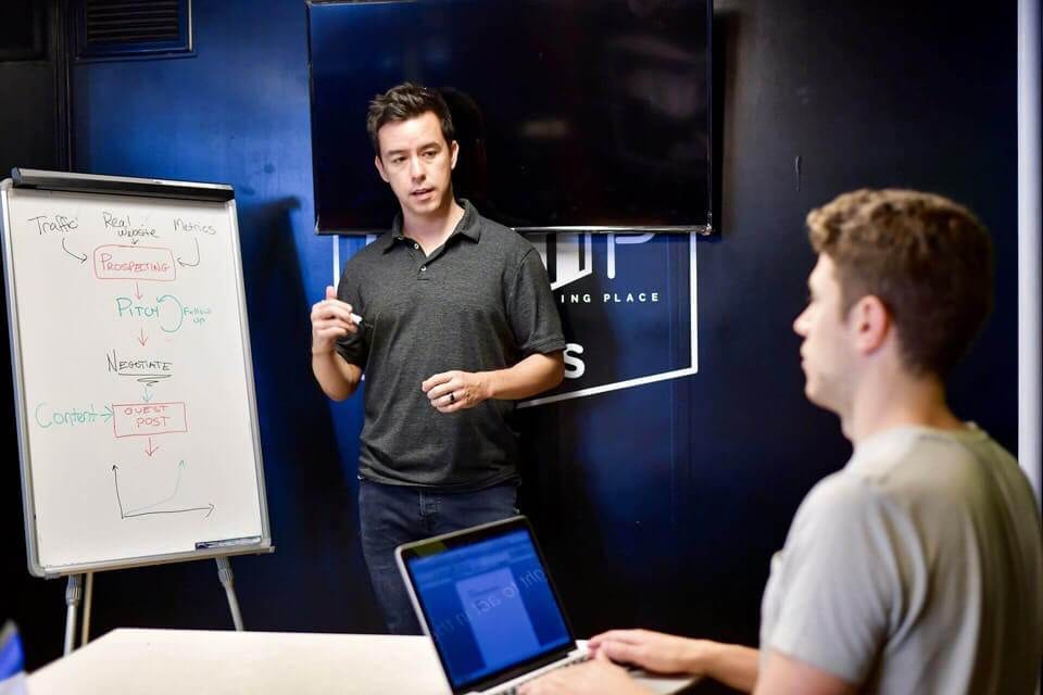 A man standing in front of a whiteboard, discussing how to create a successful affiliate marketing structure for long term income.