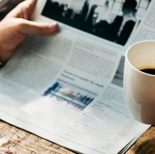 a person newsjacking their way to followers and sales while reading a newspaper with a cup of coffee.