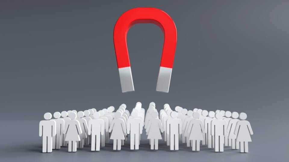 a large red horseshoe magnet levitating above a group of white figures on a gray background, symbolizing lead generation or influence.