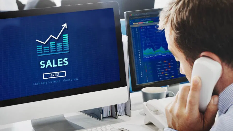 a man talking on the phone while looking at a sales graph on a computer screen, focused on increasing sales right now.