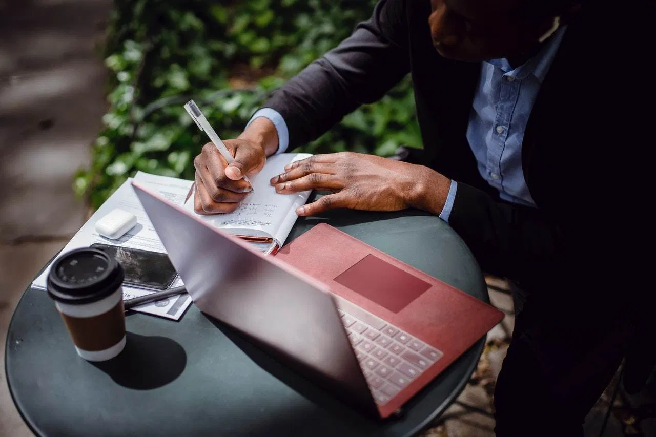 a man in a suit writing a listicle in a notebook at an outdoor table.