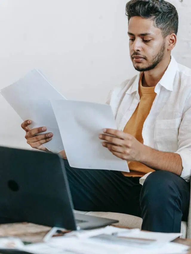 A man sitting on a couch with papers and a laptop, focusing on how to write a listicle in the proper format.