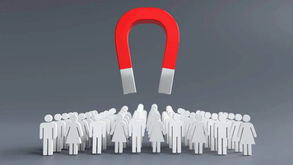 a large red horseshoe magnet levitating above a group of white figures on a gray background, symbolizing lead generation or influence.